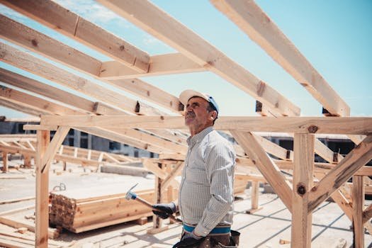 A construction worker surveys a wooden roof frame build on a sunny day.